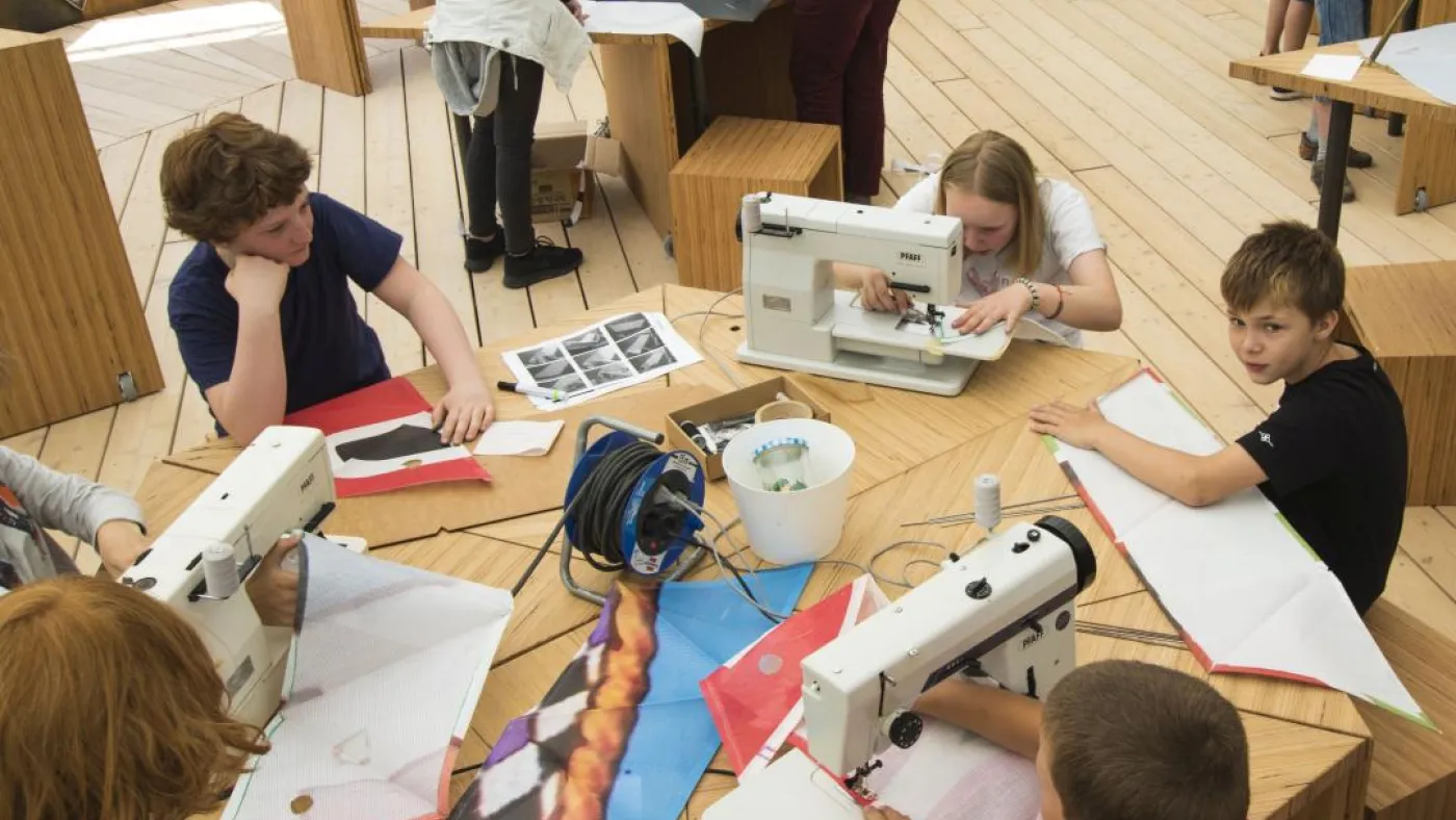 Kinder sitzen an einem Tisch mit Nähmaschinen.